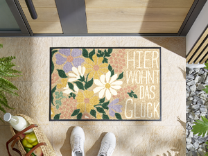 Bild in Slideshow öffnen, Fußmatte mit Blumen und Schriftzug &quot;Hier wohnt das Glück&quot; vor der Eingangstür
